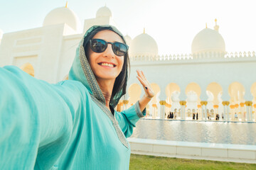 Close up woman visitor taking mobile phone photograph portrait selfie with beautiful Sheikh Zayed Grand Mosque interior in Abu Dhabi