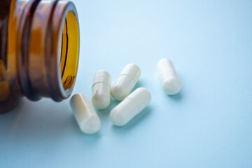 medicine pills capsule spilling out of bottle on blue background