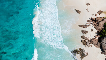 Turquoise ocean waves and white sands meeting rugged rock formations along the coast. La Digue, Seychelles.
