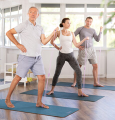 Fototapeta premium Mature man participant of Pilates marathon standing on mat perform various exercises with elastic band, expander with extension cord, and skipping rope. Athlete puts strain on muscles, trains body