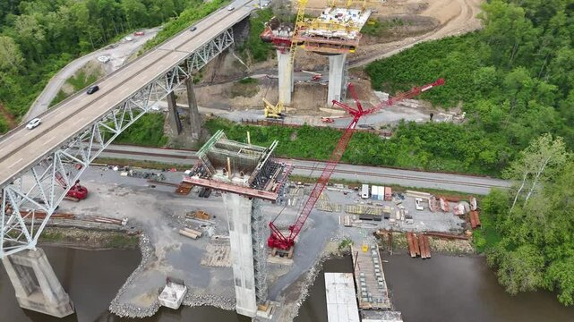 Aerial view of highway I-80 in Pennsylvania showing a bridge over a river surrounded by lush forests and mountains, with heavy traffic and massive construction of a second highway bridge nearby.