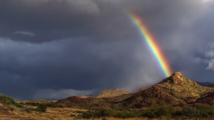 Rainbow arcs across stormy sky above rugged mountain landscape in Arizona during late afternoon