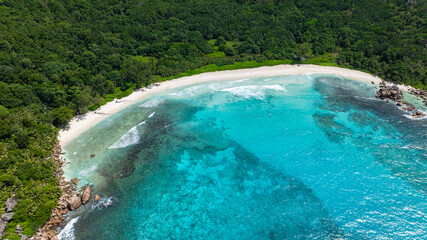 Lush island coastline surrounded by clear blue ocean waters and a rocky shore. Anse Cocos beach. La Digue, Seychelles.