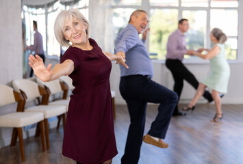 Happy elderly lady with man in elegant clothes dancing bachata in modern ballroom dance class