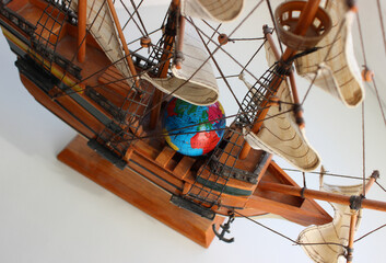 Wooden model of a sailing ship with a globe lying between the masts and sailing ropes
