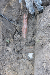 A worker wearing rubber boots standing in a deep ditch; a spade and a plastic orange pipe in marshy land next to a concrete cesspit to drain grounds