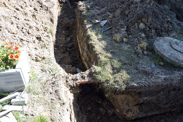 The deep ditch and a plastic orange pipe in marshy land next to a concrete cesspit to drain grounds, a hatch to a cesspit