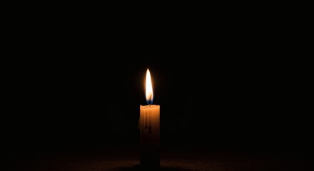 A single candle flame burning brightly in the darkness casting a soft glow around the wax candle body