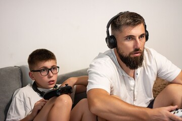 Father and son playing video games together on a couch, enjoying quality time.