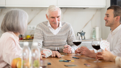 Senior man and woman play card game poker during friendly gatherings at home with middle-aged couple. Couple enthusiastically participate in game, believe in luck, collect chips, distribute winnings