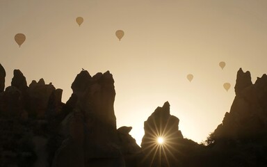The bright sun breaks through the rocky peaks in Cappadocia, Turkey. Hot air balloons. Background....