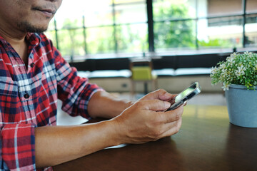 An elderly Asian man in a red plaid shirt happily uses his phone for the first time in a coffee shop.