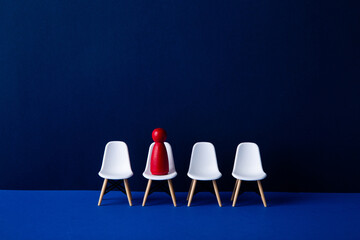 Red figurine sitting on chair leading empty white chairs on blue background: business leadership...