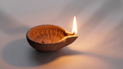 Traditional handmade clay diya with oil and flame, placed on white surface