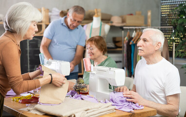 Small group of senior learners enjoying relaxed sewing class in cozy workshop, measuring, stitching, and exchanging tips in friendly social atmosphere