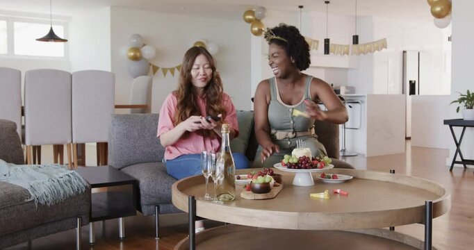 Excited by treats, diverse female friends grabbing horns, snapping selfies and laughing on couch