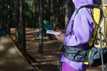 Close-up a woman with a hiking backpack and a smartphone and portable power bank in hands, against...