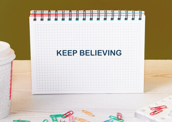 Business concept. Copy space. Concept Words KEEP BELIEVING in an open notebook surrounded by...