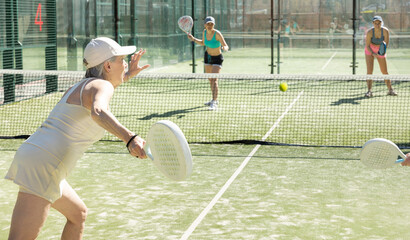 Dynamic old woman playing Padel Tennis in pairs in the open air tennis court