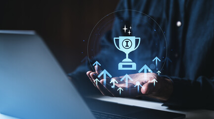 Digital trophy icon hovering above open hands with growth arrows and laptop on dark background, symbolizing success and achievement in business technology. © ImageFlow