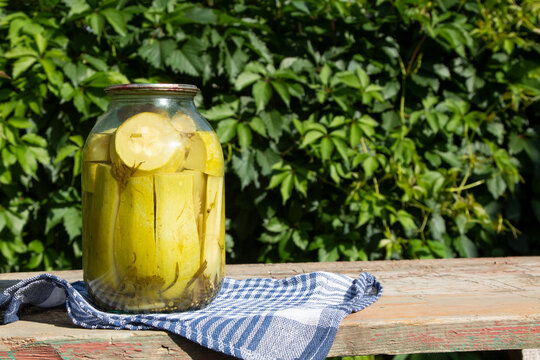 Jar of farm canned zucchini on wooden table in garden. Pickled home vegetables. Copy space. 