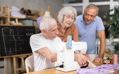 Enthusiastic older adults, women and men, gathering around sewing machine in training workshop...