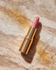 Luxurious lipstick with golden glitter accents rests on marble surface, exuding elegance and glamour. shimmering pink hue adds touch of sophistication to any makeup collection
