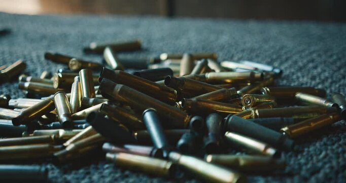 Spent bullet casings fall onto a textured carpet surface at shooting range
