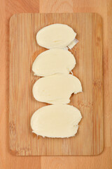 A top-down shot shows four slices of fresh mozzarella cheese arranged on a light wooden cutting board