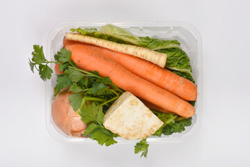 fresh soup vegetables, including carrots, parsley, celery, onion, and parsnip, packaged in a clear plastic container