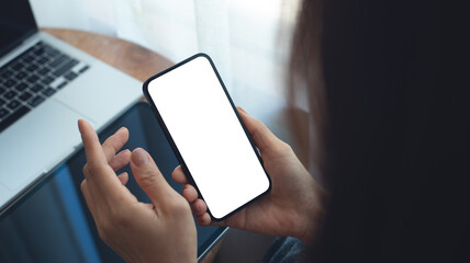 Mockup, Woman using mobile phone with blank white screen while online working on laptop at coffee shop. Business woman using smartphone, mockup for social media marketing, closeup