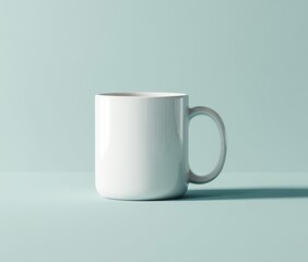 Obraz premium A simple, white ceramic mug sits on a pale teal surface, casting a subtle shadow, against a matching backdrop