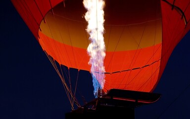 Obraz premium Strong flames inflate a bright red hot air balloon. A flight in Cappadocia. Turkey travel. Flames of a large fire and a balloon glowing in the dark. Tourist tour, Turkish culture, majestic journey