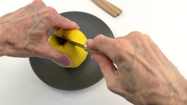 primo piano di mela gialla ssu piatto in ceramica e coltello con mani che tagliano la mela