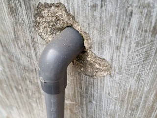 Close-up of damaged wall with exposed gray PVC pipes and peeling textured surface