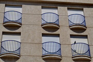 Façade blanche avec balcons semi circulaires bleus. Volets Fermés.