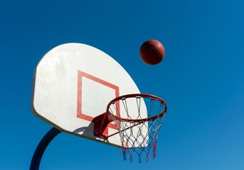 Basketball in flight towards hoop against a clear blue sky