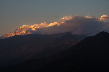 A breathtaking view of the snow-capped peaks Annapurna South and Machapuchare when the clouds softly hug the mountains in great Himalayas in Nepal.