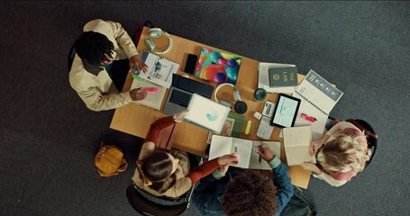 Studying, group and exchanging notes in library, above and students with tech for knowledge and app. Education, people and learning for exam in university, planning and preparing test with books - Powered by Adobe