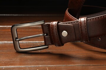 One brown leather belt on wooden table, closeup