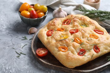 Delicious focaccia with tomatoes and spices on gray textured table, closeup