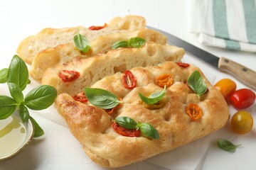 Cut delicious focaccia with tomatoes, basil, oil and knife on light table, closeup
