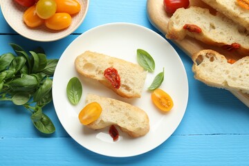 Pieces of delicious focaccia with tomatoes and basil on light blue wooden table, flat lay