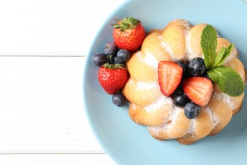 Tasty Bundt cake with powdered sugar and berries on white wooden table, top view. Space for text