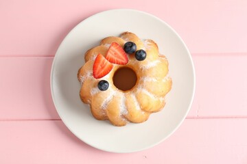 Tasty Bundt cake with powdered sugar and berries on pink wooden table, top view.