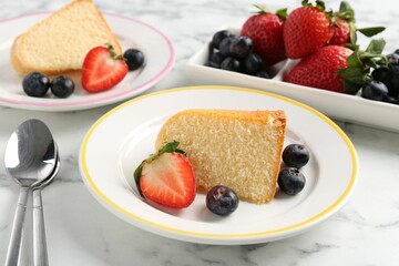Pieces of tasty bundt cake with berries on white marble table, closeup