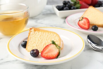 Pieces of tasty bundt cake with berries and tea on white marble table, closeup