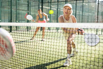 Sportive elderly woman engaged in Padel Tennis in open-air court of tennis club