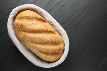 Loaf of bread with sesame seeds in basket on black textured table, top view. Space for text