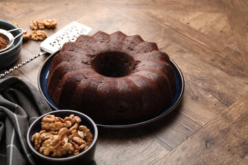 Tasty chocolate bundt cake, walnuts and cocoa powder on wooden table, closeup. Space for text